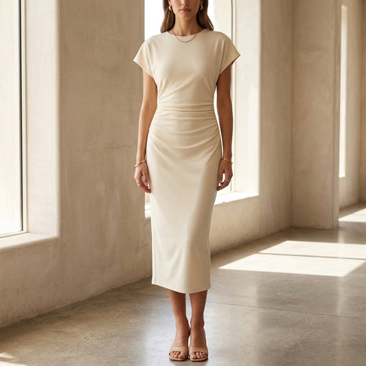 Full-body shot of an elegant female model wearing the beige Aurelia midi dress in a bright, sunlit minimalist architectural interior, natural soft daylight, showing the flattering draped silhouette and elegant midi length.